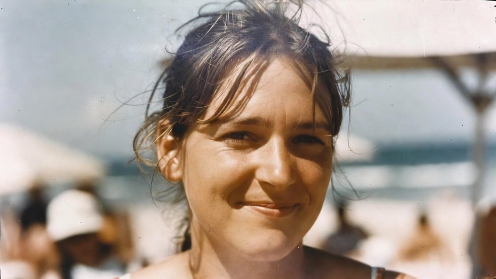 Foto einer jungen Frau am Strand, sie lächelt in die Kamera